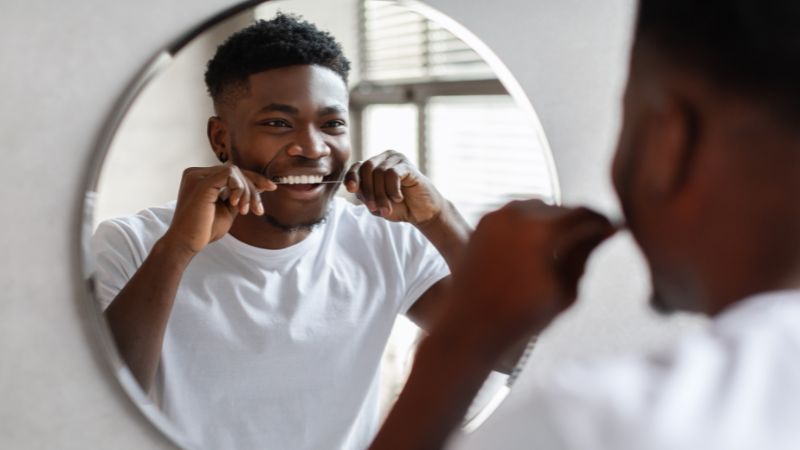 Homem usando fio dental para prevenir problemas periodentais.